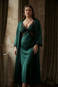 Woman wearing a green satin dress with a matching robe in a warm-toned room.